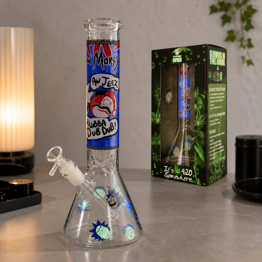 Bong de cristal con base cónica, tubo decorado con dibujos y cazoleta lateral, sobre una mesa junto a su caja.