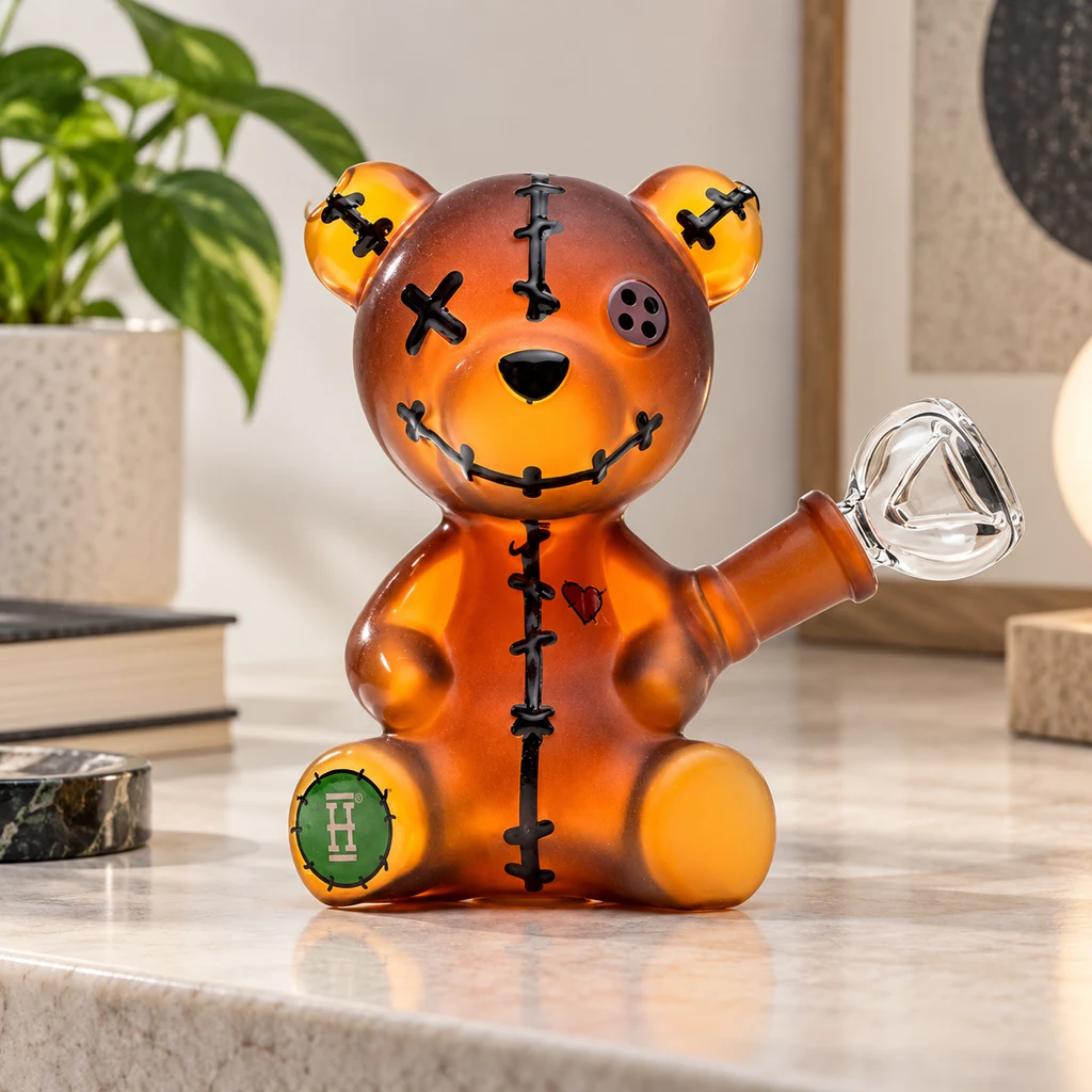 Bong con forma de oso naranja, costuras negras, un ojo de botón y otro en cruz, con cazoleta transparente lateral.
