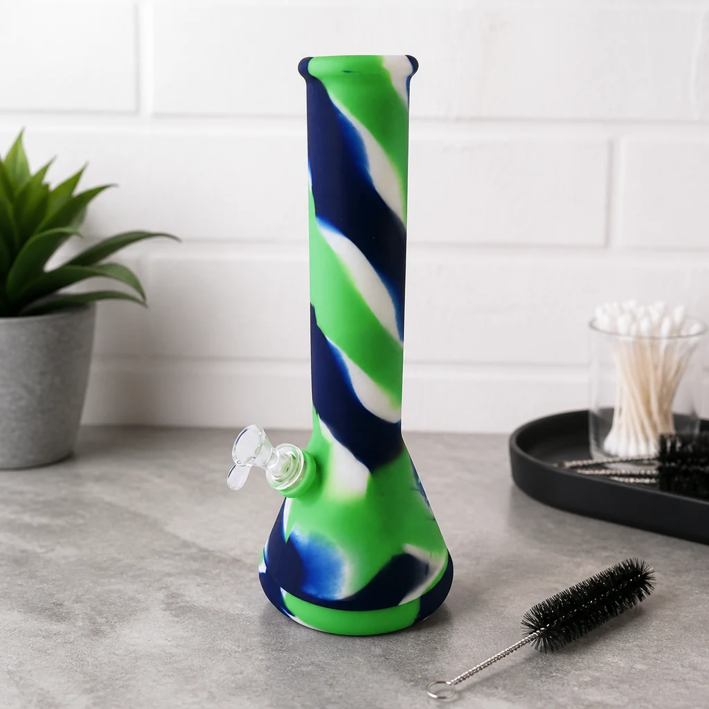 Bong de silicona con franjas verdes, azules y blancas y cazoleta transparente, sobre una encimera junto a un cepillo de limpieza.