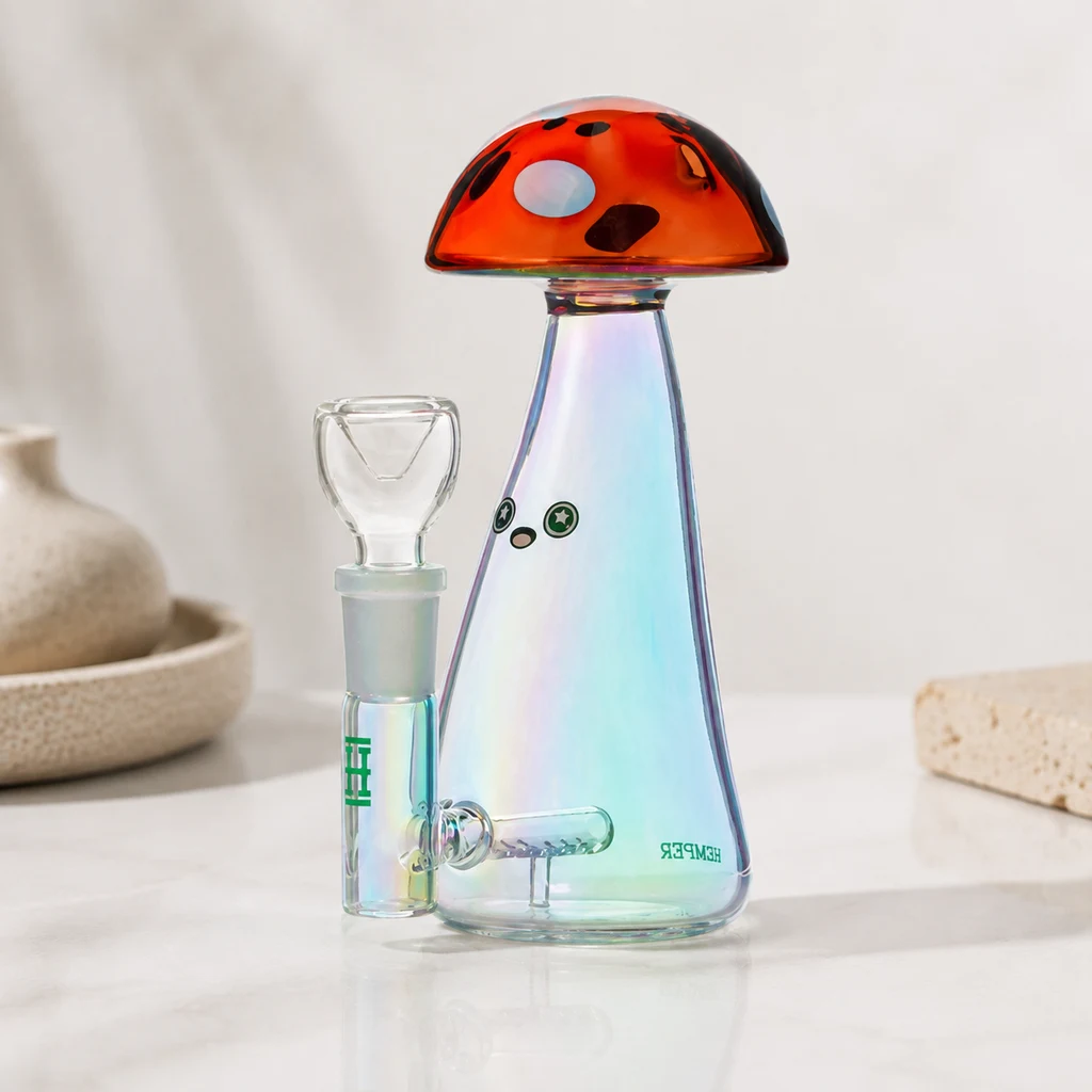 Bong Hemper Trippy Shroom sobre una mesa, con cuerpo iridiscente, remate de seta naranja con manchas y cazoleta lateral transparente.