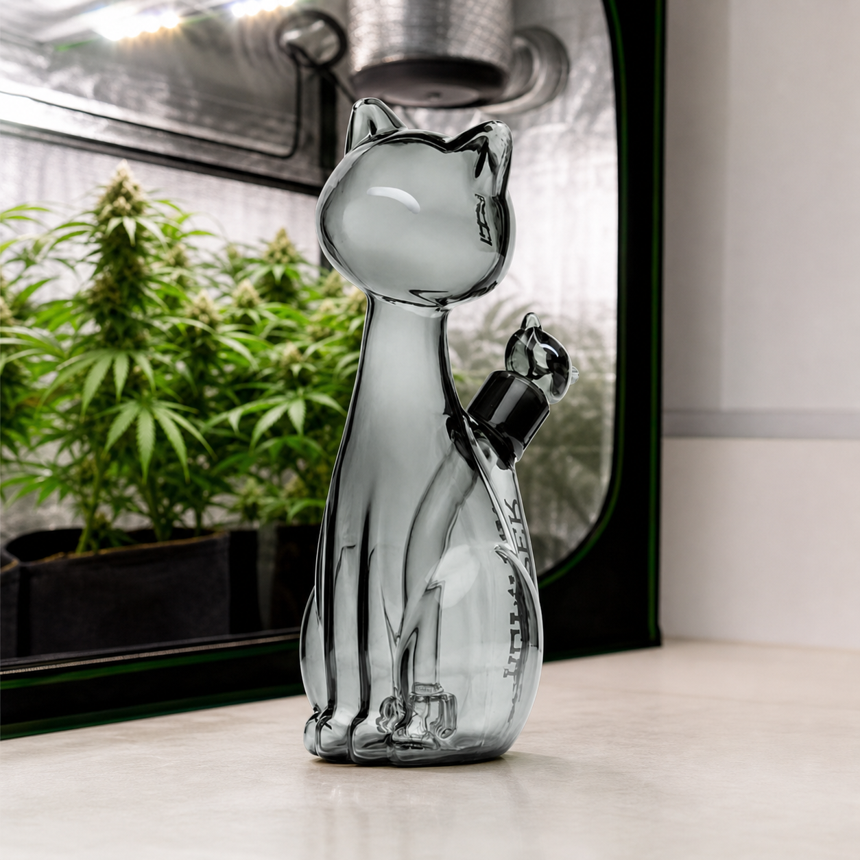 Bong Hemper Alleycat XL de vidrio con forma de gato y cazoleta lateral, sobre una mesa ante un armario con plantas de cannabis.