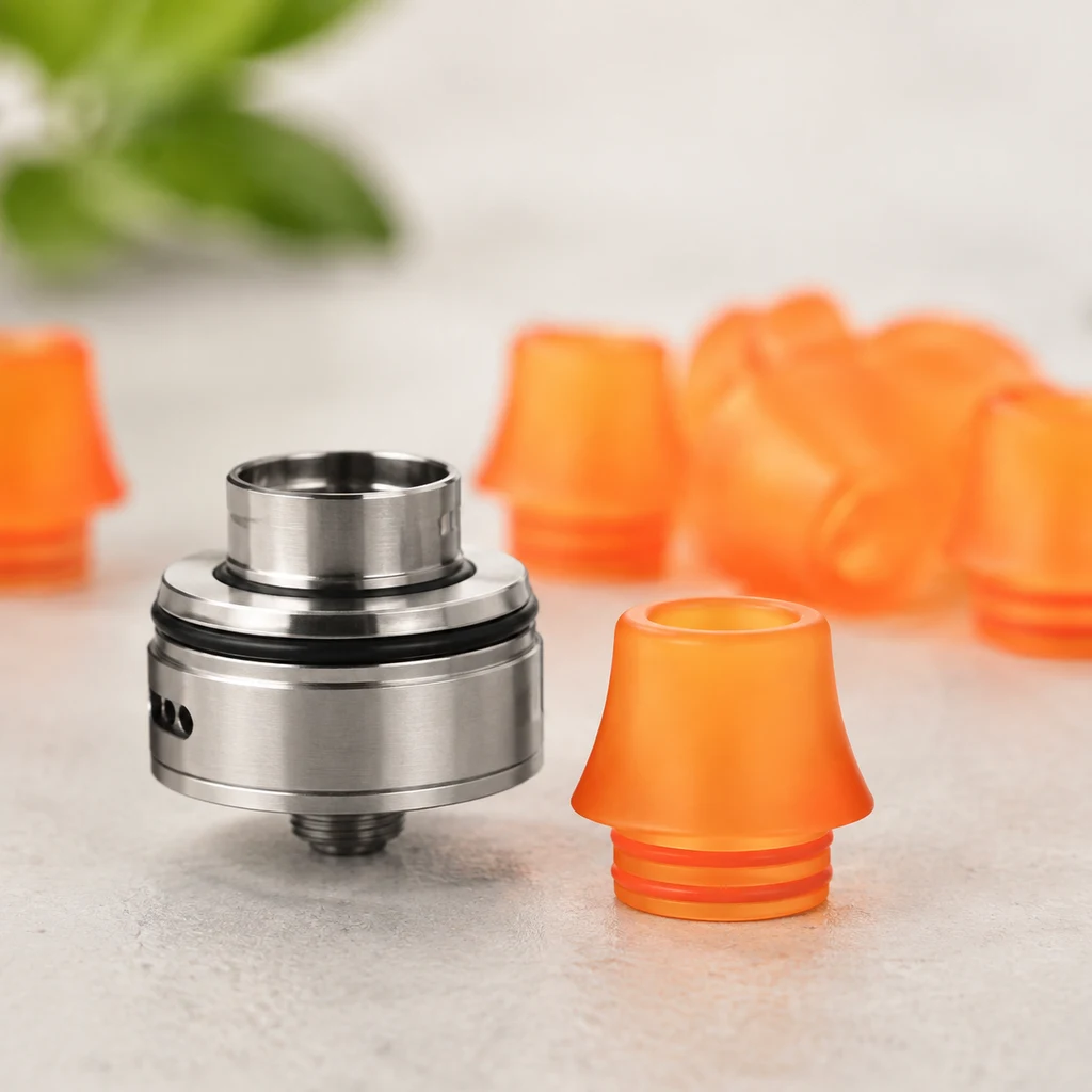 Boquilla naranja de base acanalada junto a un componente metálico de vapeo, con varias boquillas desenfocadas al fondo.