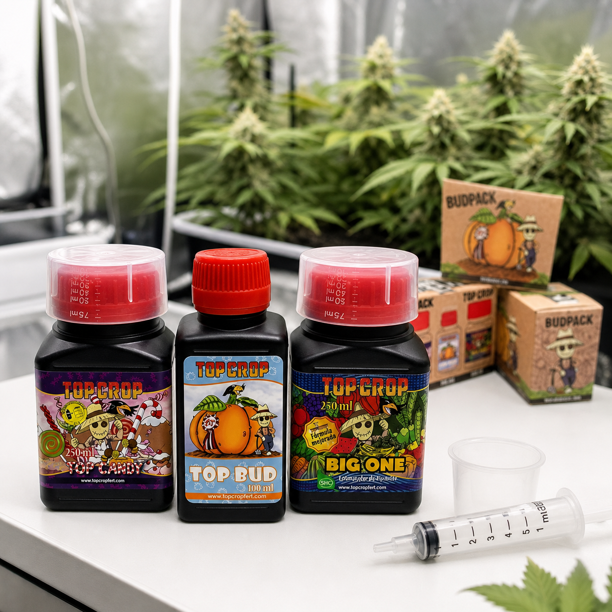 Botes Top Candy, Top Bud y Big One de Top Crop junto a una jeringa, vaso dosificador y cajas Budpack, con plantas al fondo. Botes Top Candy, Top Bud y Big One de Top Crop junto a una jeringa, vaso dosificador y cajas Budpack, con plantas al fondo.