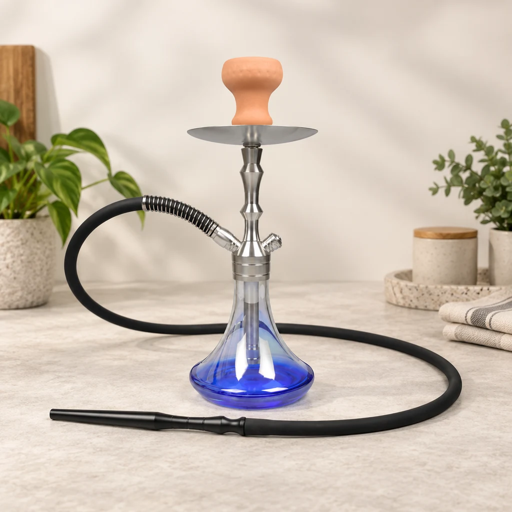 Cachimba Aladin MVP360 con base transparente azul, cuerpo plateado, cazoleta naranja y manguera negra sobre una encimera junto a plantas.