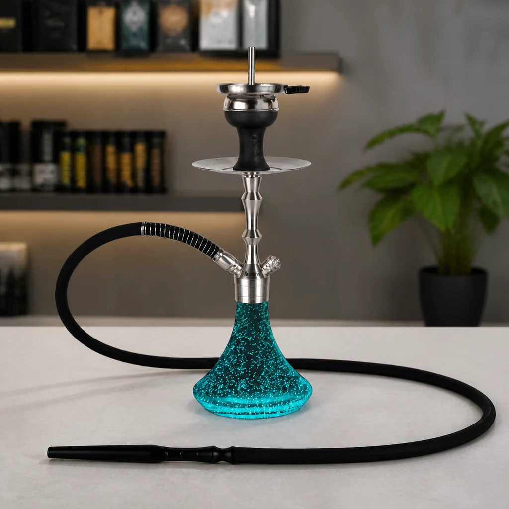 Cachimba Aladin MVP 360 con base turquesa moteada, cuerpo plateado y manguera negra extendida sobre una encimera, con estantes y una planta al fondo.