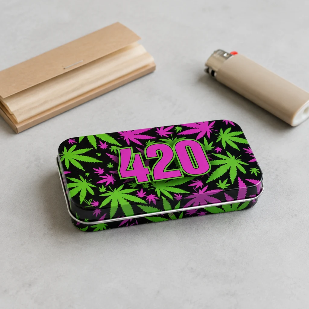 Caja rectangular negra con hojas verdes y fucsias y el número 420, sobre una mesa gris junto a papel de liar y un mechero beige.