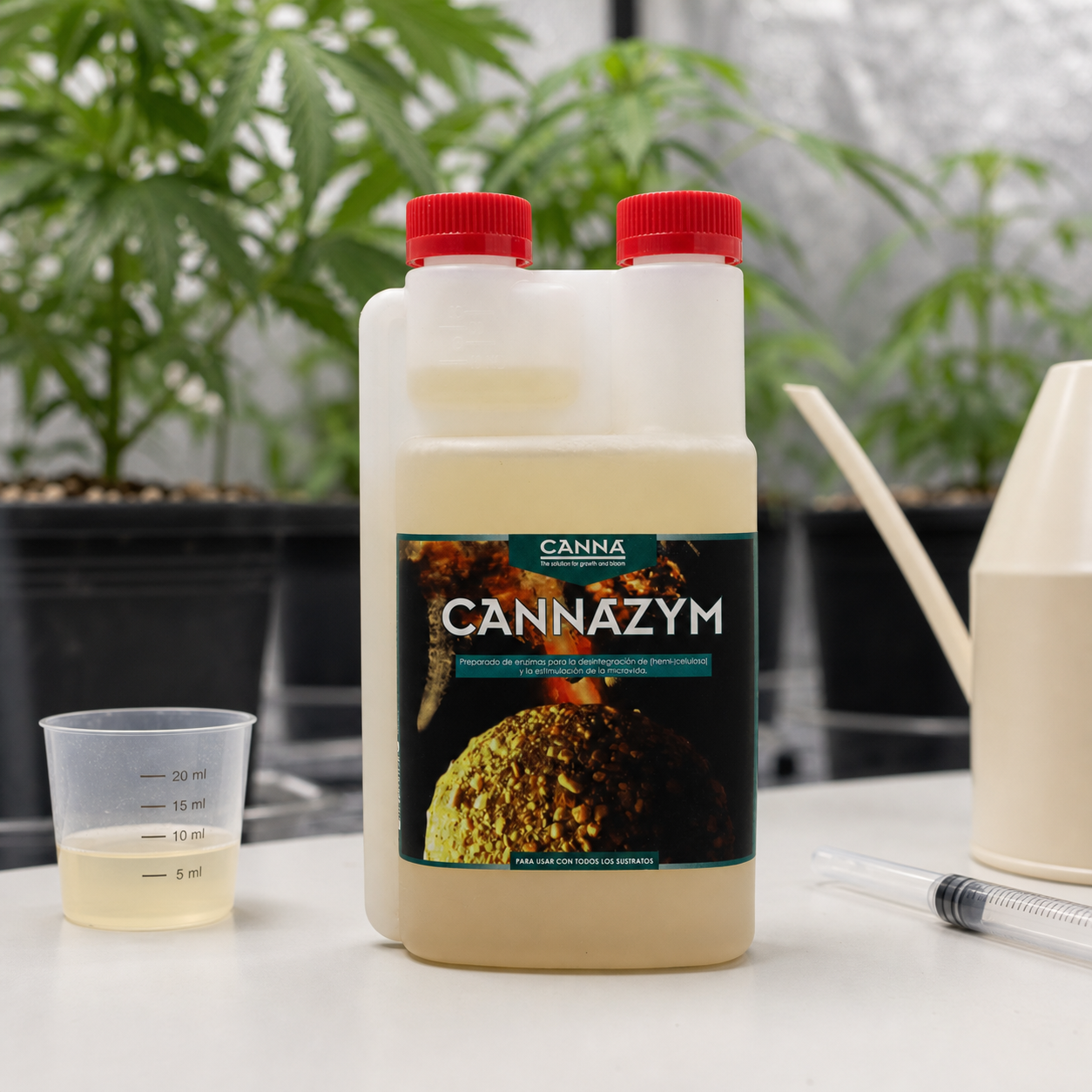 Envase de Canna Cannazym con tapones rojos, junto a un vaso medidor con líquido y una jeringa, con plantas al fondo.