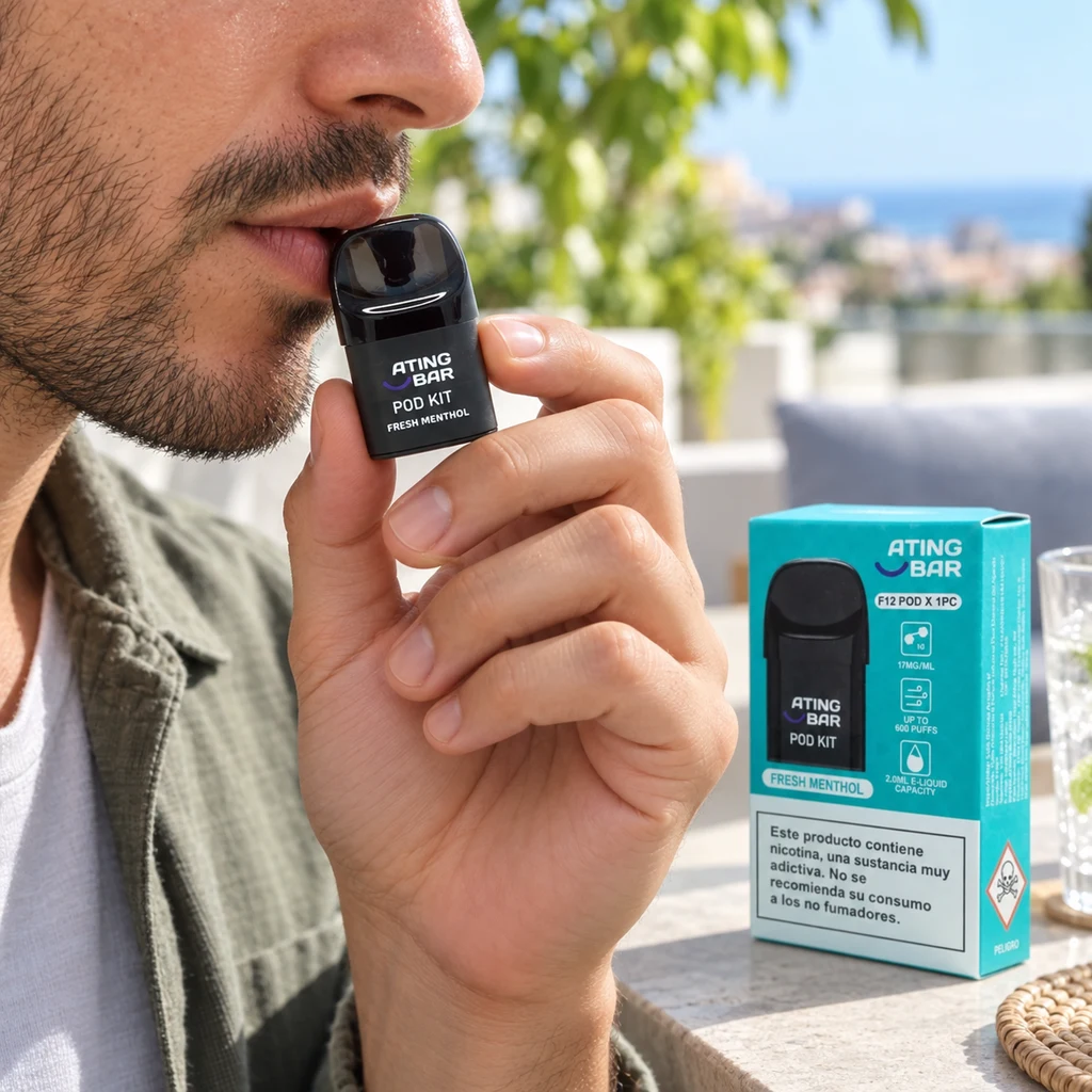 Hombre con un dispositivo negro Ating Bar Fresh Menthol junto a los labios y una caja turquesa sobre la mesa de una terraza.