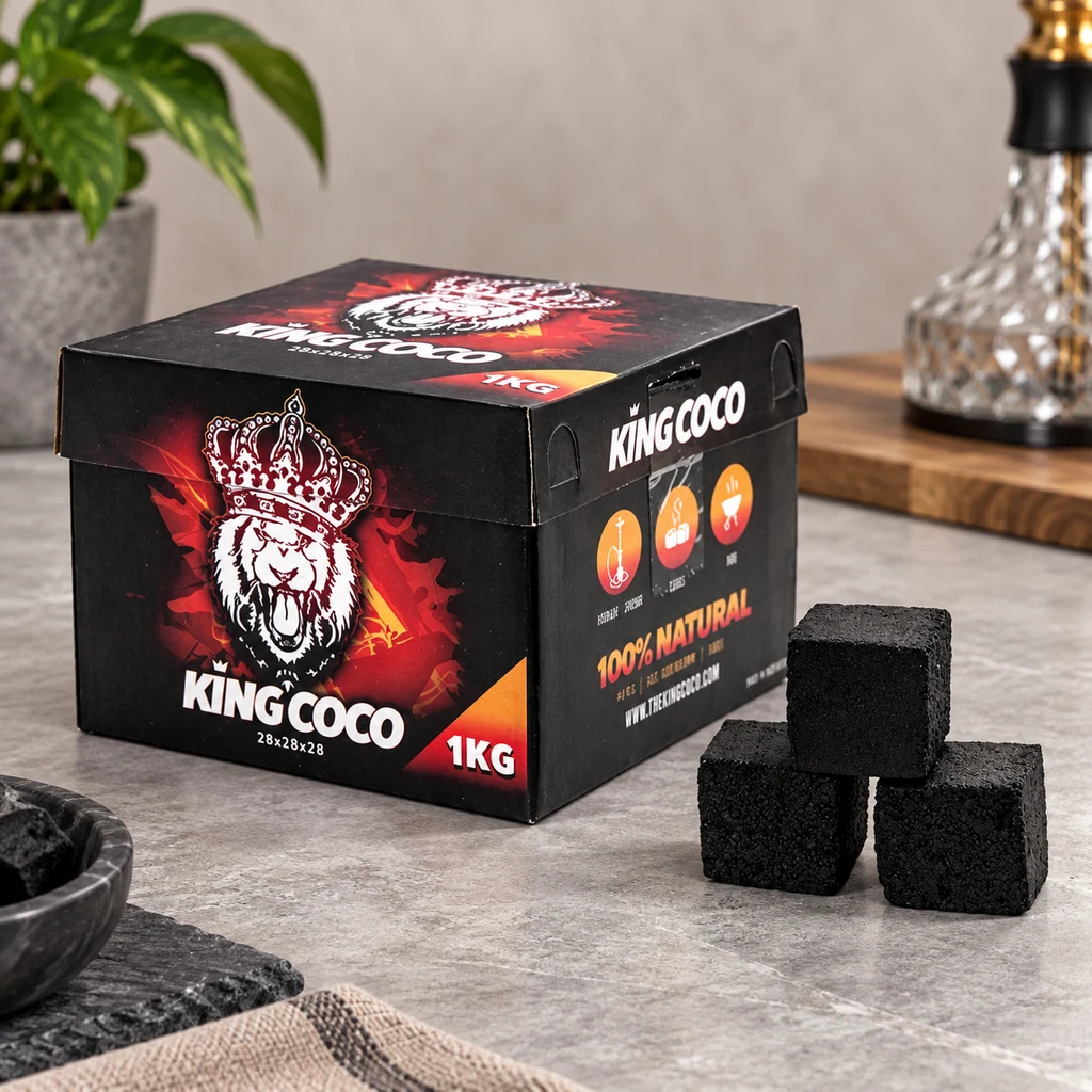 Caja negra y roja de carbón King Coco, rotulada 1 kg y decorada con un león coronado, junto a varios cubos negros sobre una encimera. Caja negra y roja de carbón King Coco, rotulada 1 kg y decorada con un león coronado, junto a varios cubos negros sobre una encimera.