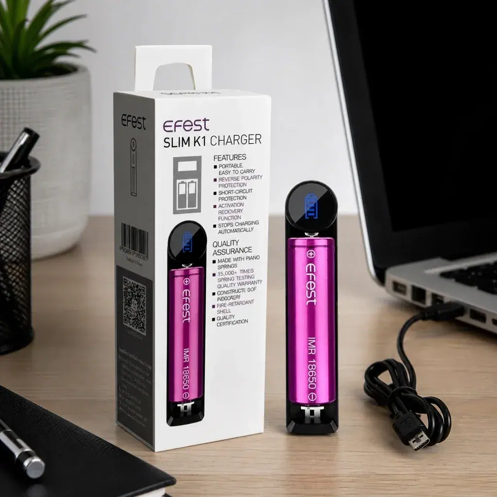 Cargador EFEST SLIM K1 con batería rosa e indicador azul, junto a su caja y un cable USB sobre un escritorio con portátil.
