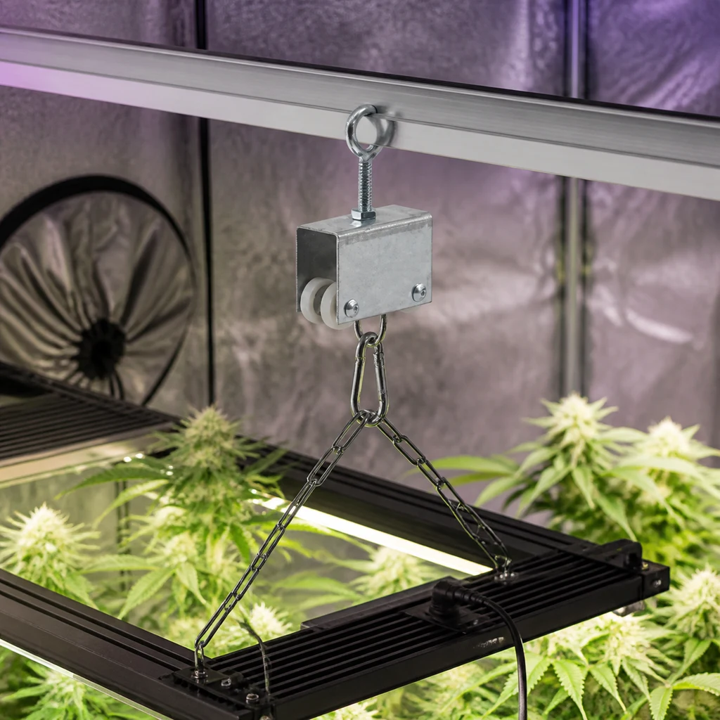Carro auxiliar Light Rail sobre un riel horizontal, con mosquetón y cadenas que sostienen una luminaria sobre plantas en un armario de cultivo.