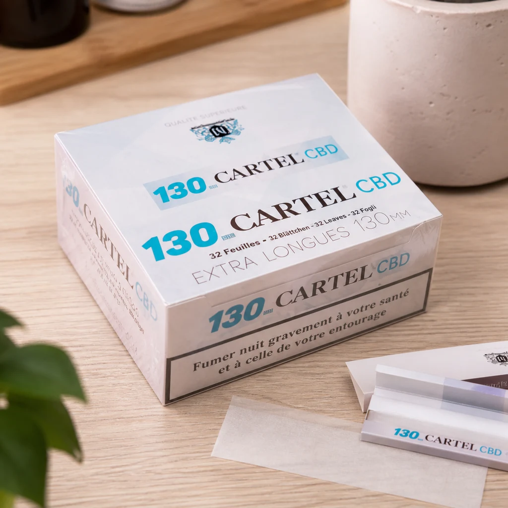 Caja de papel de liar Cartel CBD con la inscripción 130 mm, junto a un librillo abierto y una hoja translúcida sobre una mesa de madera.