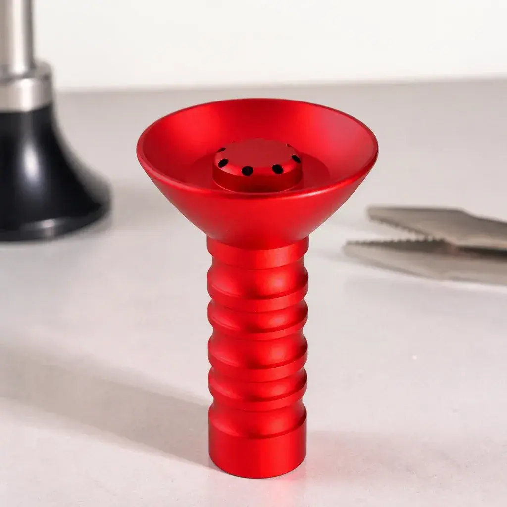 Cazoleta HORUS roja con copa ancha, orificios centrales y pie acanalado, sobre una mesa con pinzas y parte de una cachimba al fondo.