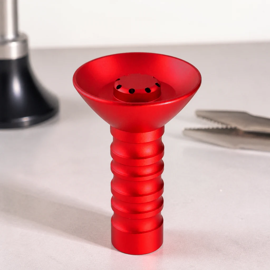 Cazoleta HORUS roja con copa ancha, orificios centrales y pie acanalado, sobre una mesa con pinzas y parte de una cachimba al fondo.