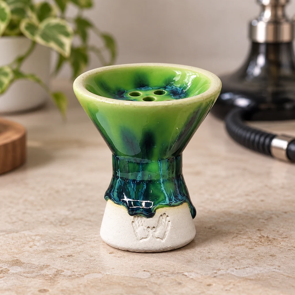 Cazoleta Tempo Jade con esmalte verde y azul, orificios centrales y base clara, sobre una encimera con una cachimba al fondo.