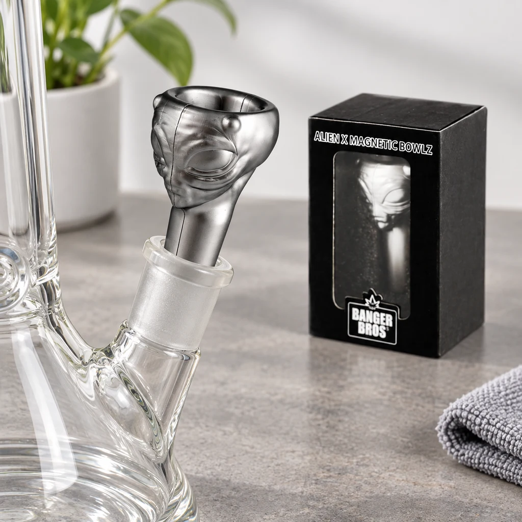Escena generada de una cazoleta plateada con rostro de alienígena, colocada en un bong transparente junto a una caja negra Banger Bros.