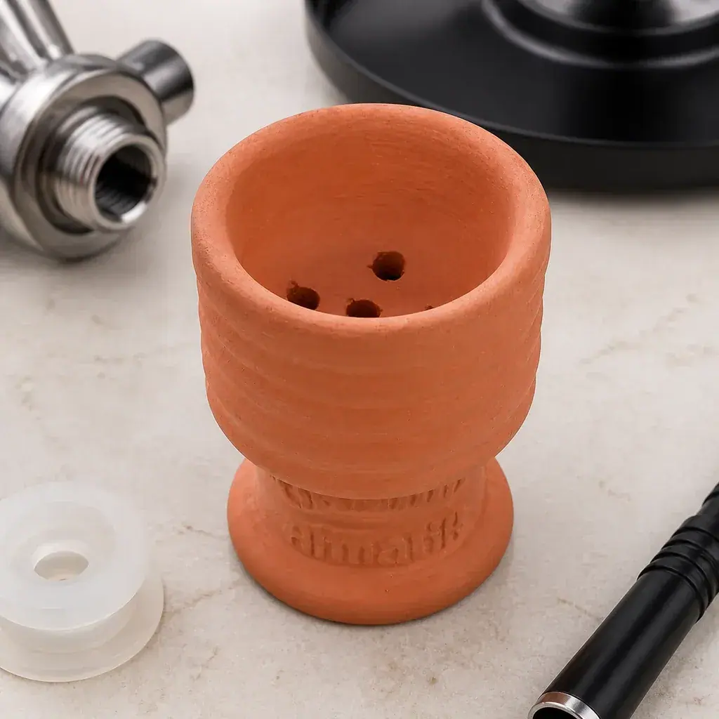 Cazoleta de cachimba de barro rojizo, vista desde arriba en ángulo, con varios orificios interiores y accesorios alrededor.