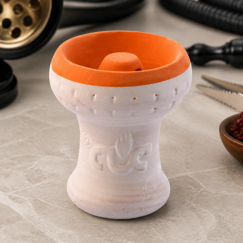 Cazoleta de cachimba blanca con borde e interior naranjas y elevación central, sobre una mesa junto a accesorios de cachimba.