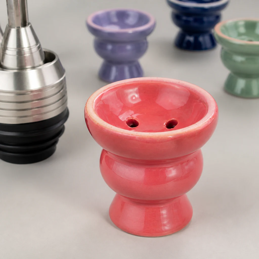 Cazoleta de cerámica coral con orificios visibles, junto a una pieza metálica de cachimba y otras cazoletas de distintos colores.