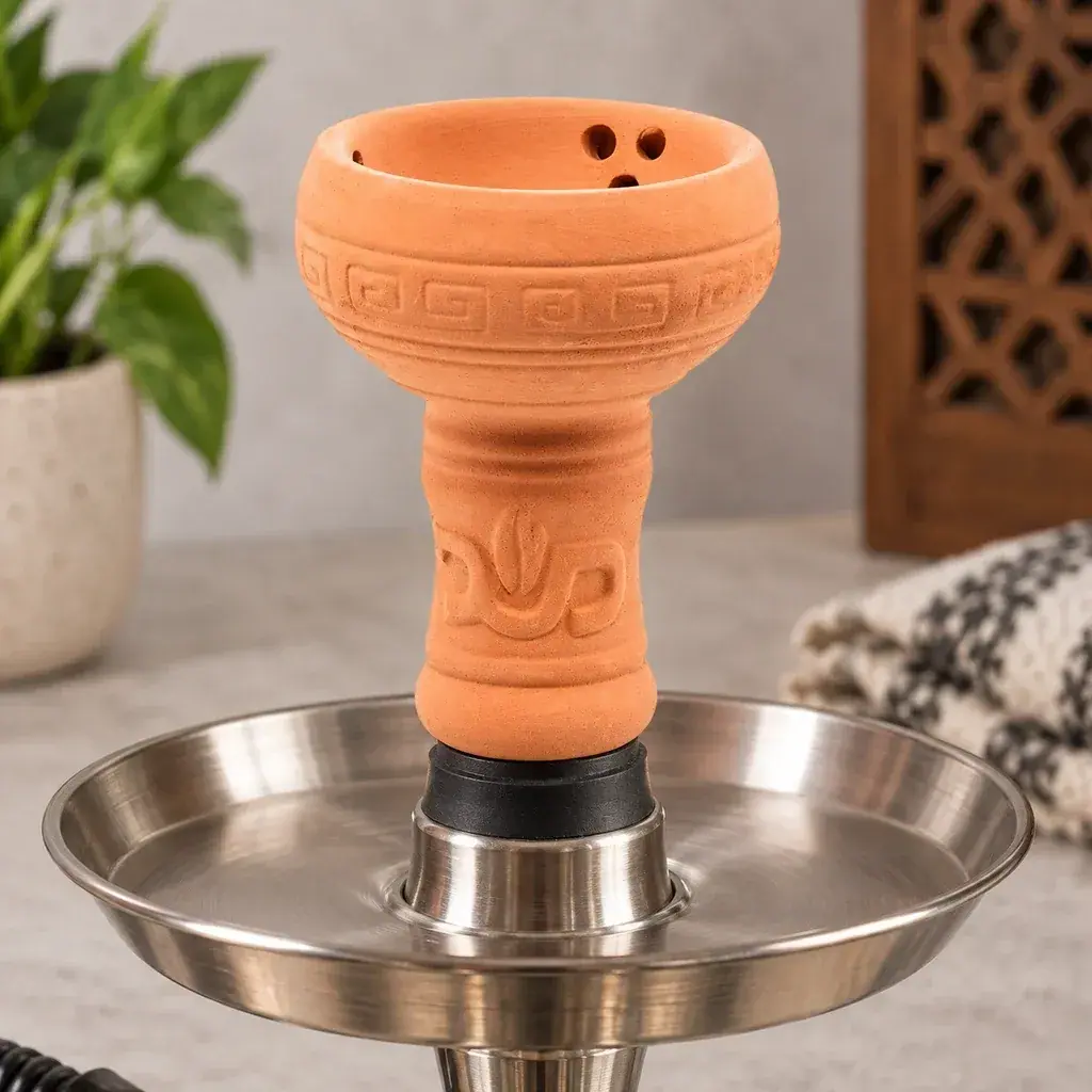 Cazoleta de arcilla naranja con motivos geométricos y orificios interiores, montada sobre el plato metálico de una cachimba.