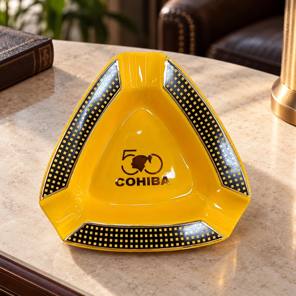 Cenicero amarillo Cohiba triangular, con tres apoyos para puros, bordes de cuadros negros y dorados y logotipo central.