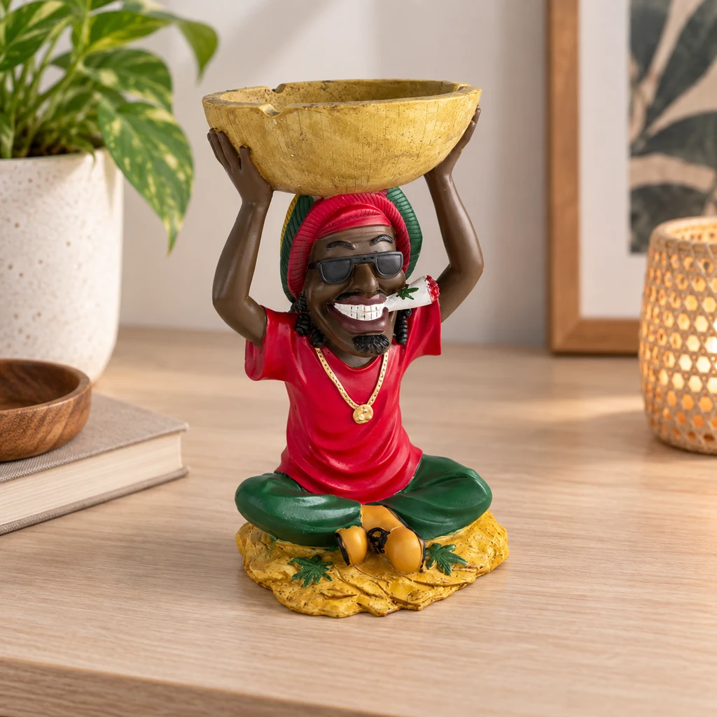 Cenicero con figura sentada de camiseta roja, gafas oscuras y gorro multicolor que sostiene un cuenco amarillo sobre la cabeza.