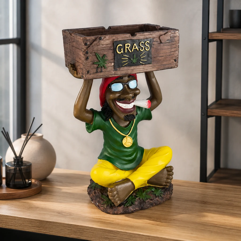 Escena generada de un cenicero con figura rasta sentada que sostiene una caja con el rótulo GRASS, sobre una mesa.