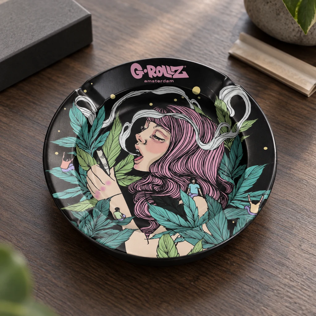 Cenicero negro G-Rollz Colossal Dream sobre una mesa, decorado con una mujer de pelo rosa, hojas verdes y volutas blancas.