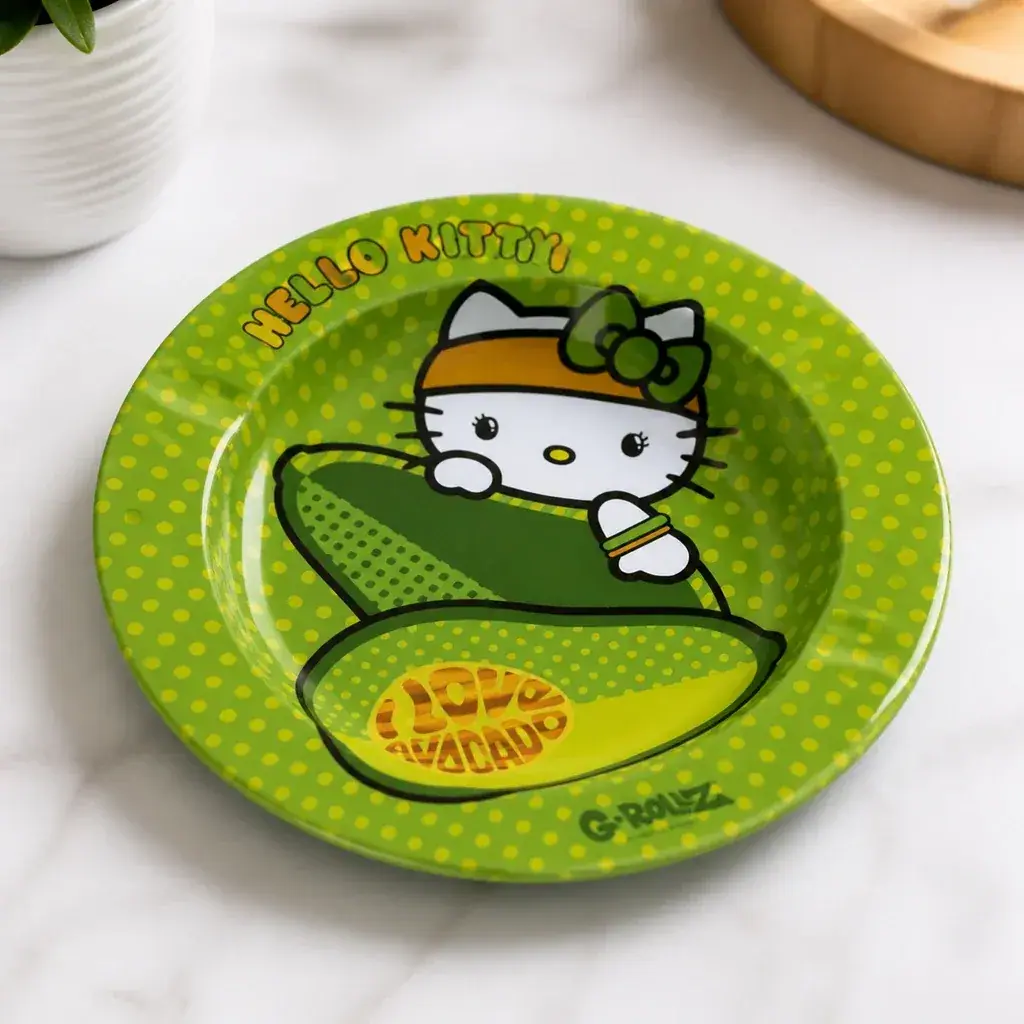 Cenicero verde de Hello Kitty con dibujos de aguacates y lunares amarillos, sobre una superficie clara junto a una maceta.