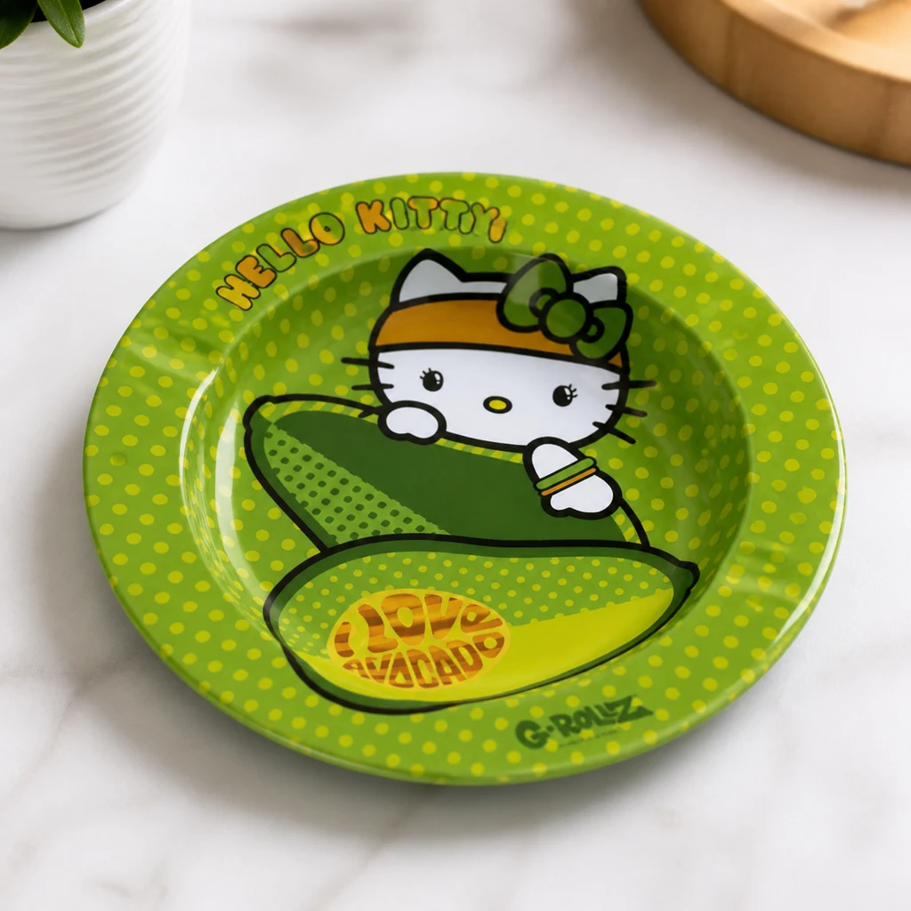 Cenicero verde de Hello Kitty con dibujos de aguacates y lunares amarillos, sobre una superficie clara junto a una maceta.