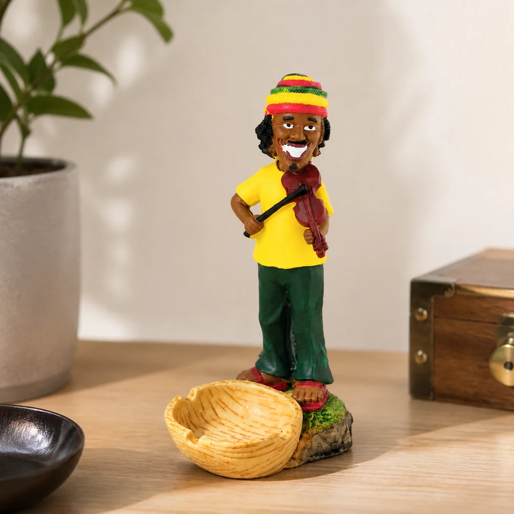 Cenicero con figura de violinista con gorro multicolor, camiseta amarilla y pantalones verdes, junto a un cuenco sobre una mesa. Cenicero con figura de violinista con gorro multicolor, camiseta amarilla y pantalones verdes, junto a un cuenco sobre una mesa.