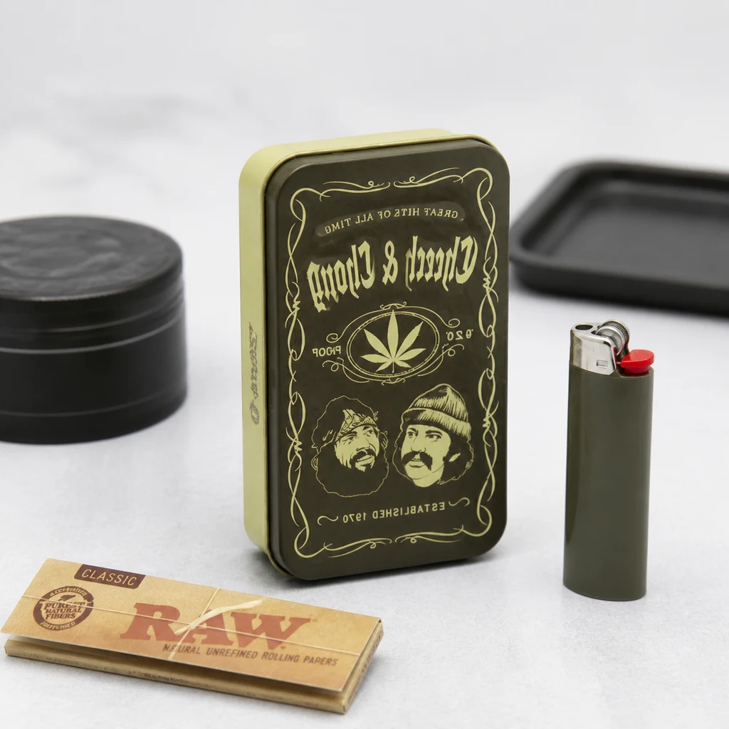 Caja Cheech & Chong de pie con retratos y motivos dorados, junto a un encendedor, un grinder y un librillo de papel RAW. Caja Cheech & Chong de pie con retratos y motivos dorados, junto a un encendedor, un grinder y un librillo de papel RAW.
