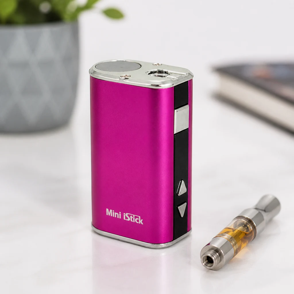 Eleaf Mini iStick de color fucsia con botones laterales y conexión superior, junto a un cartucho separado sobre una mesa blanca.