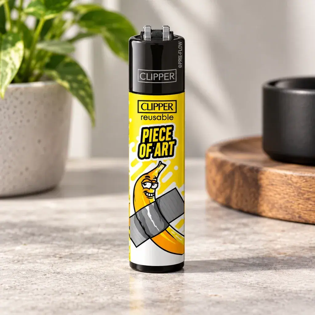 Clipper Classic Bananas amarillo con cabezal negro y dibujo de un plátano sujeto con cinta gris, de pie sobre una encimera. Clipper Classic Bananas amarillo con cabezal negro y dibujo de un plátano sujeto con cinta gris, de pie sobre una encimera.
