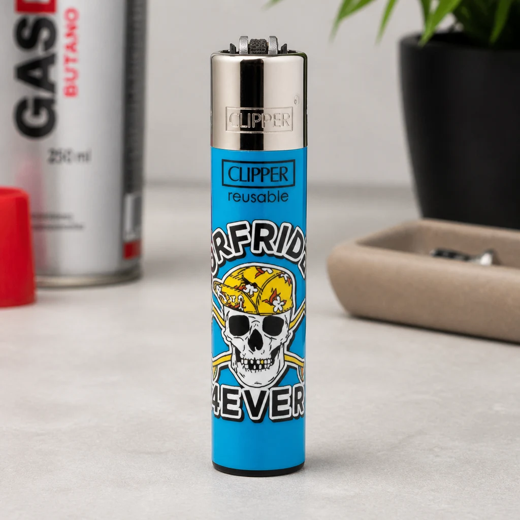 Mechero Clipper Classic Skullttoo azul con calavera y pañuelo amarillo, de pie sobre una mesa junto a un cenicero. Mechero Clipper Classic Skullttoo azul con calavera y pañuelo amarillo, de pie sobre una mesa junto a un cenicero.