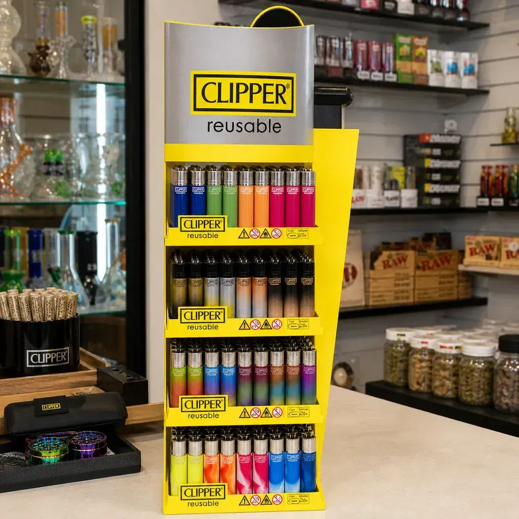 Expositor amarillo Clipper con varias filas de mecheros de distintos colores y diseños sobre el mostrador de una tienda en una escena generada.