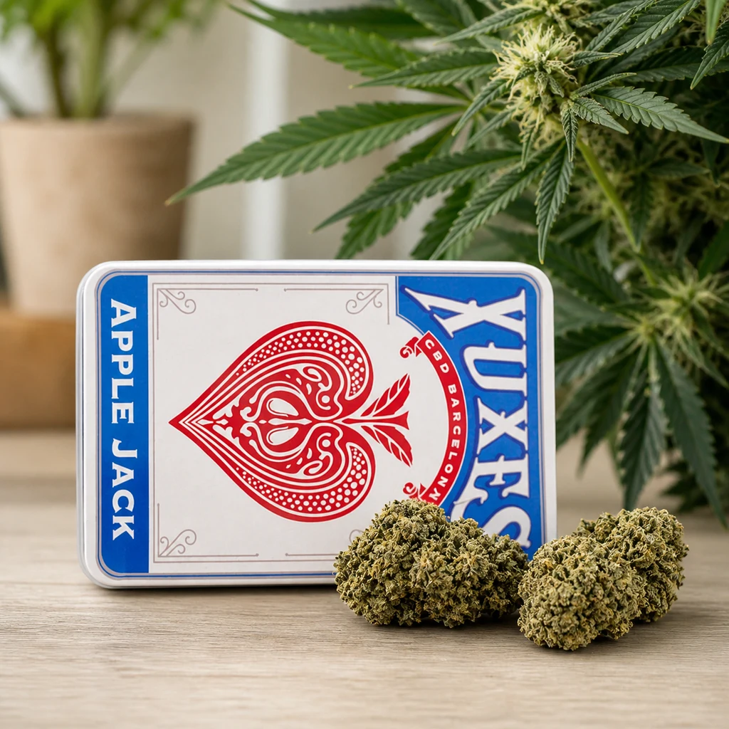Lata de Xuxes Apple Jack con diseño de as de picas, junto a varios cogollos sobre una mesa y una planta al fondo.