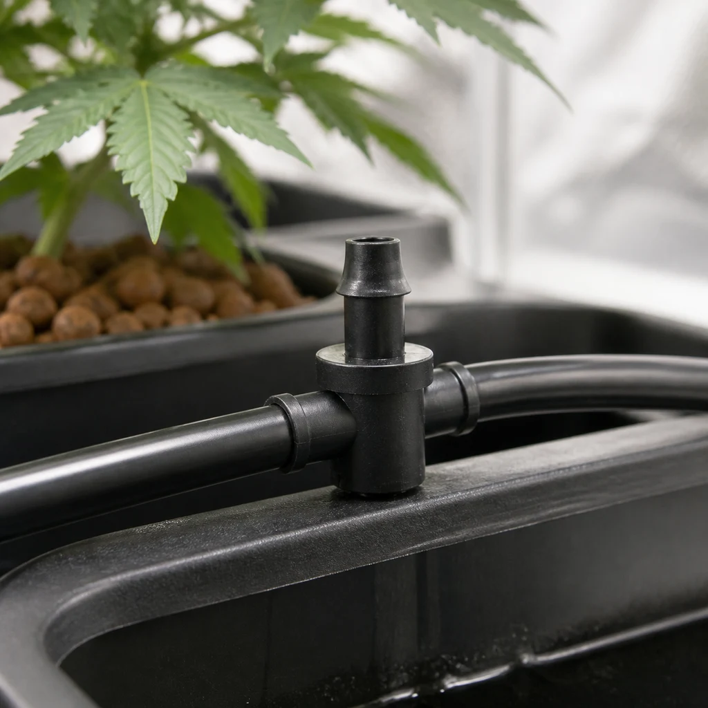Escena generada de un conector negro en T entre dos tramos de tubo, con una salida vertical abierta junto a una maceta con planta.