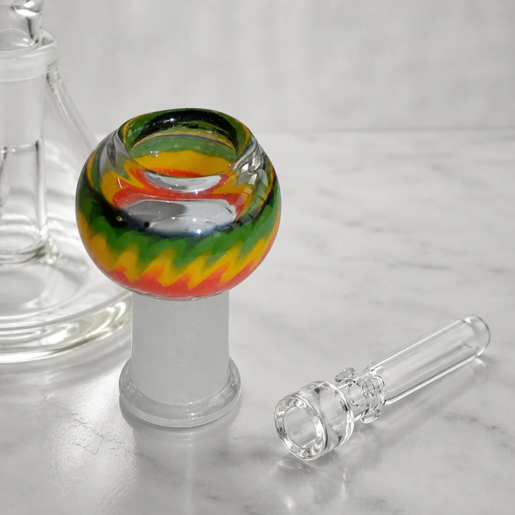 Cúpula de bong redondeada con franjas verdes, amarillas y rojas, junto a un clavo transparente y parte de un bong.