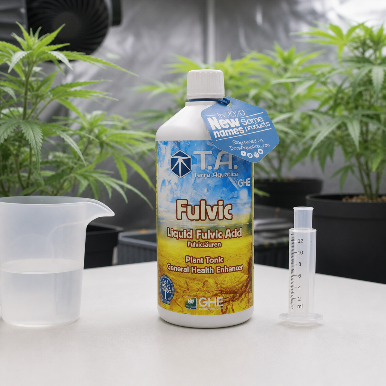 Botella de Fulvic Terra Aquatica GHE sobre una mesa, junto a una jarra con líquido y un dosificador, con plantas al fondo. Botella de Fulvic Terra Aquatica GHE sobre una mesa, junto a una jarra con líquido y un dosificador, con plantas al fondo.