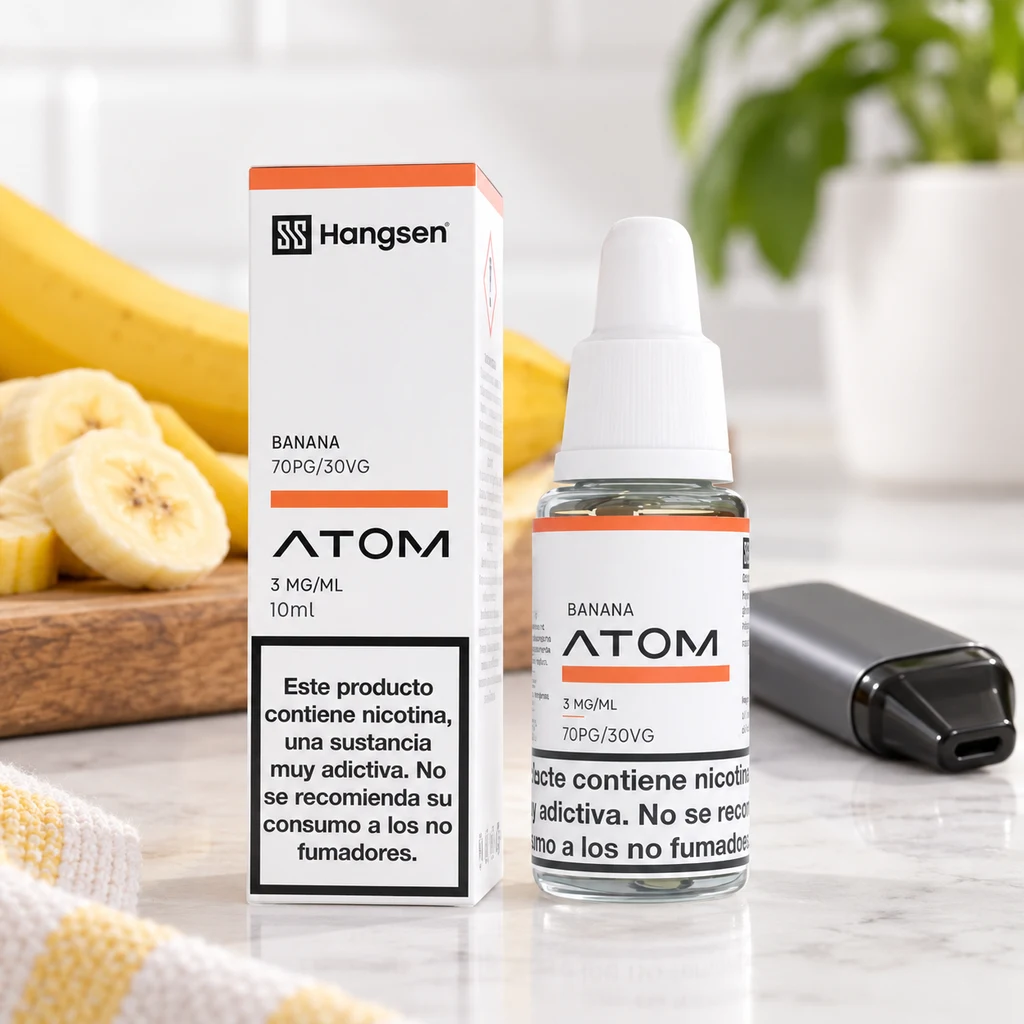 Frasco y caja de Hangsen Atom Banana con etiqueta de 3 mg/ml, junto a un vapeador gris y plátano cortado sobre una encimera.