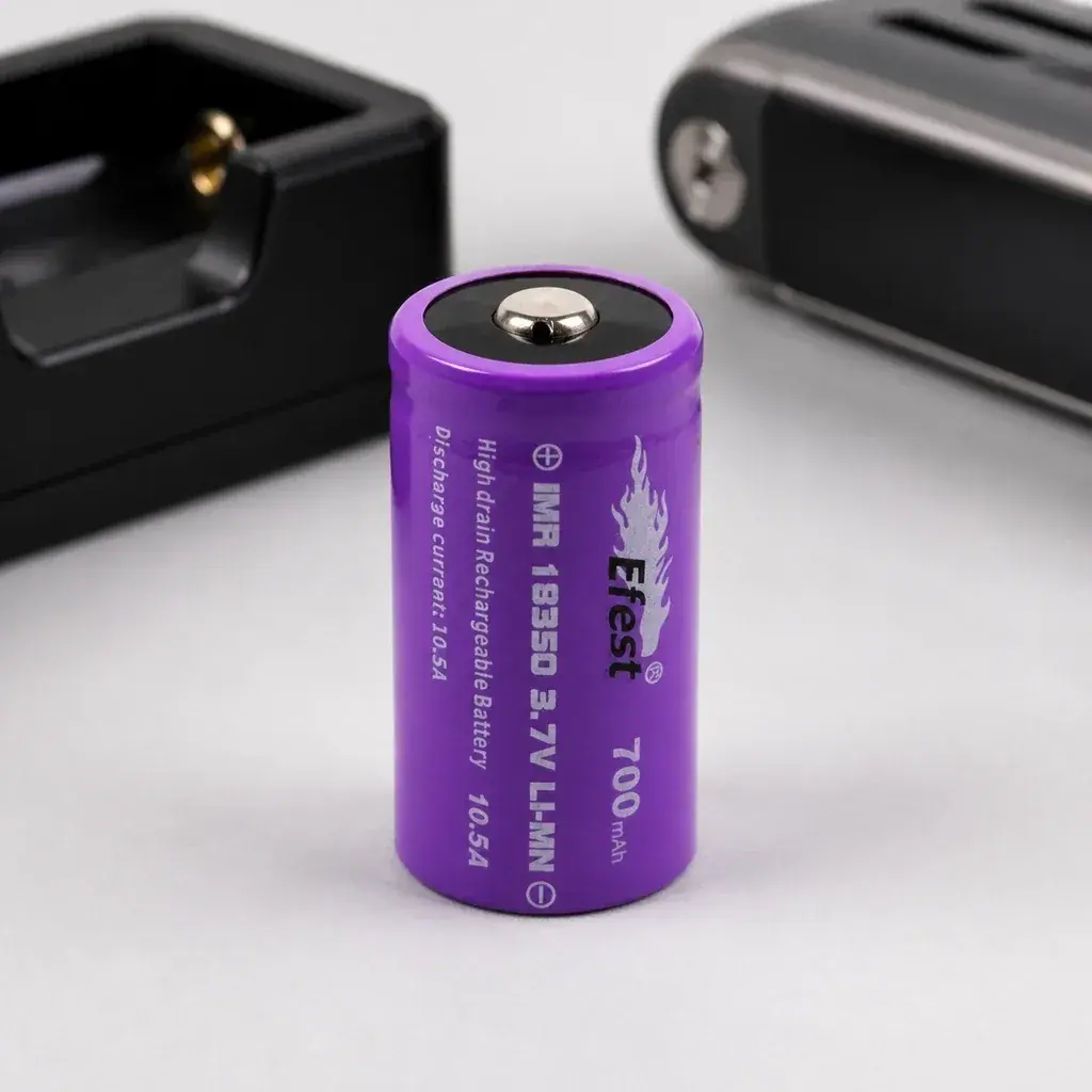 Batería morada Efest IMR 18350 en posición vertical, con polo positivo visible e indicaciones de 3,7 V y 700 mAh; cargador al fondo.
