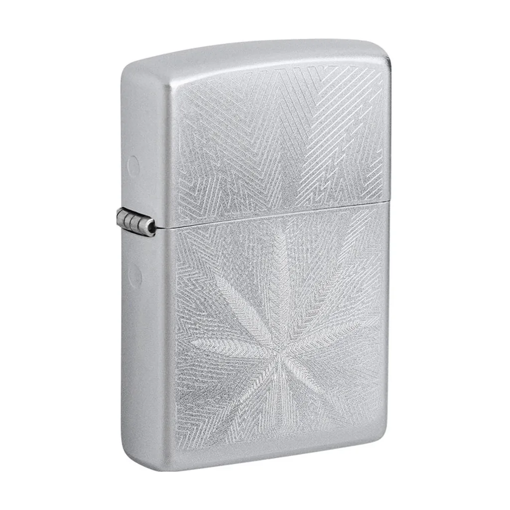Encendedor Zippo cerrado de acabado plateado, visto en ángulo, con una hoja de cannabis grabada entre finas líneas geométricas.