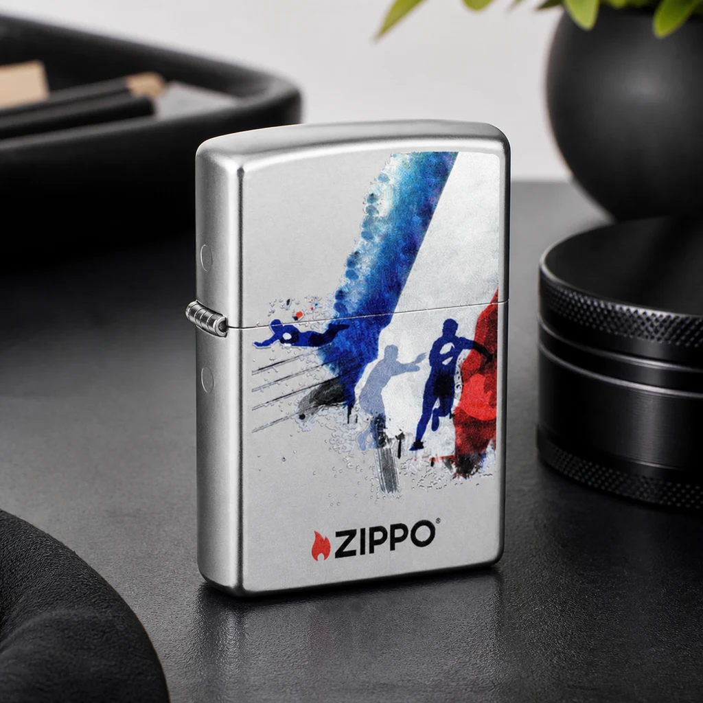 Encendedor Zippo plateado cerrado, con siluetas de jugadores de rugby y trazos azules y rojos, sobre una mesa oscura.