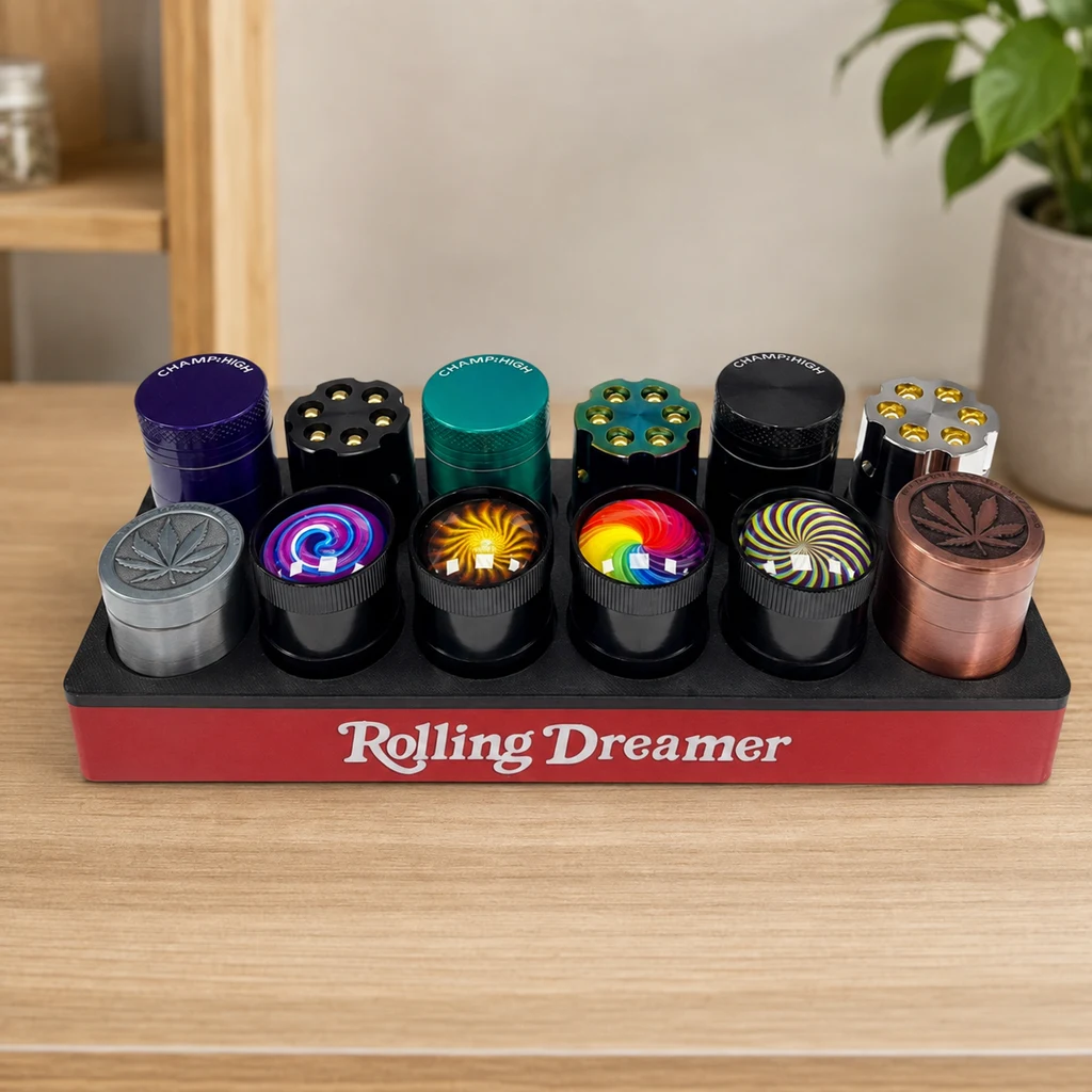 Expositor Rolling Dreamer sobre una mesa con varios modelos de grinders en distintos colores, con hojas, espirales y otros dibujos en las tapas.