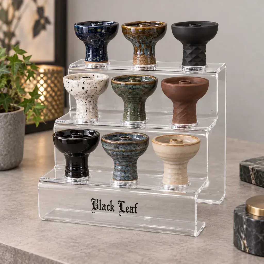 Soporte transparente escalonado con inscripción Black Leaf y varias cazoletas de cachimba de distintos colores y acabados sobre una encimera.