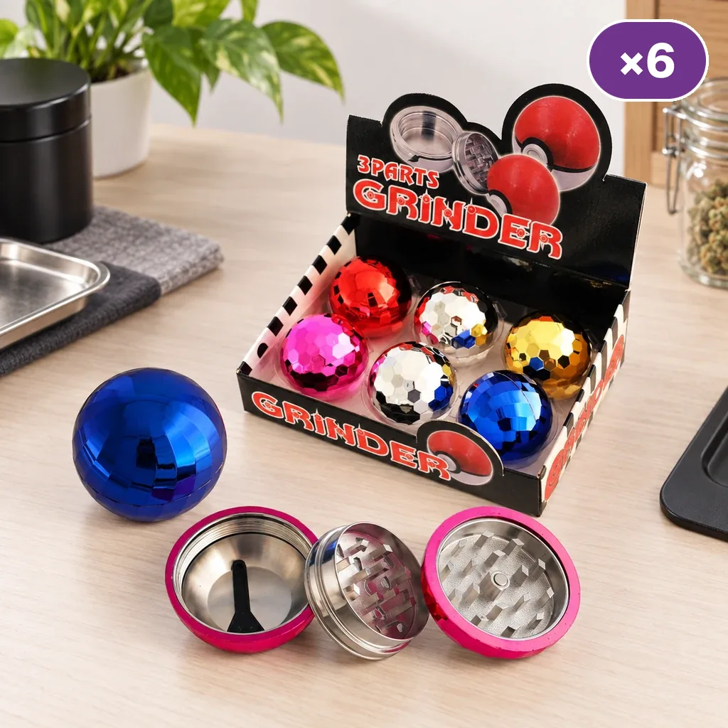 Grinders esféricos facetados de colores en un expositor sobre una mesa, con un modelo rosa desmontado y otro azul cerrado delante.