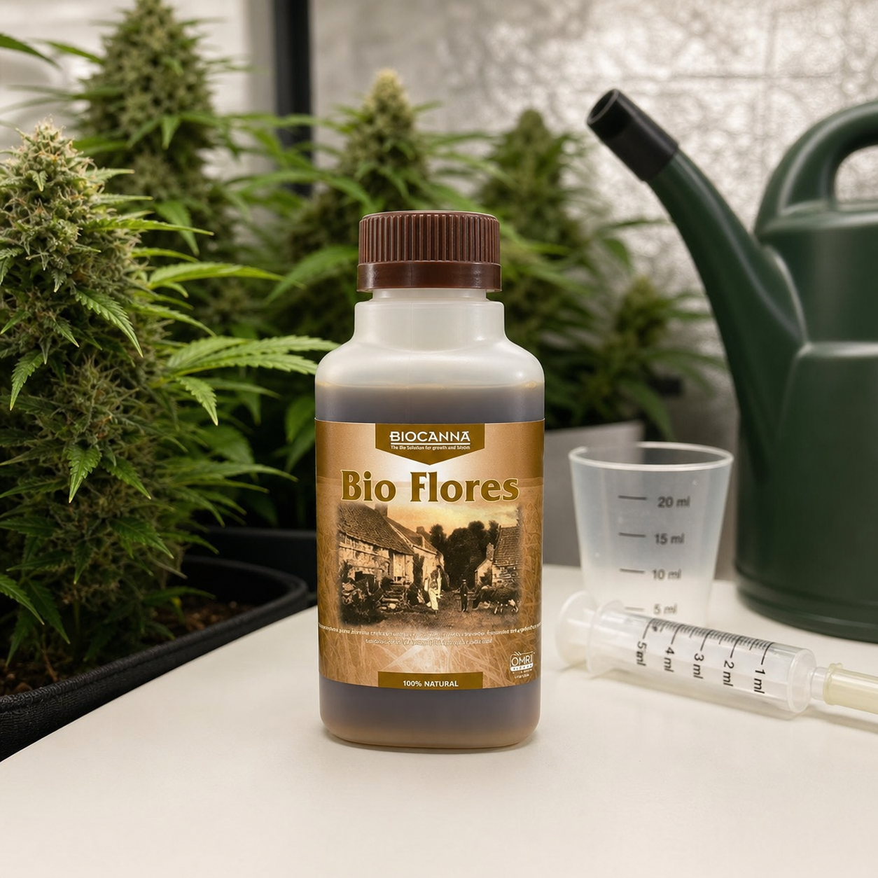 Botella de Bio Flores de Biocanna junto a un vaso medidor y una jeringa, con una regadera y plantas de cannabis al fondo.