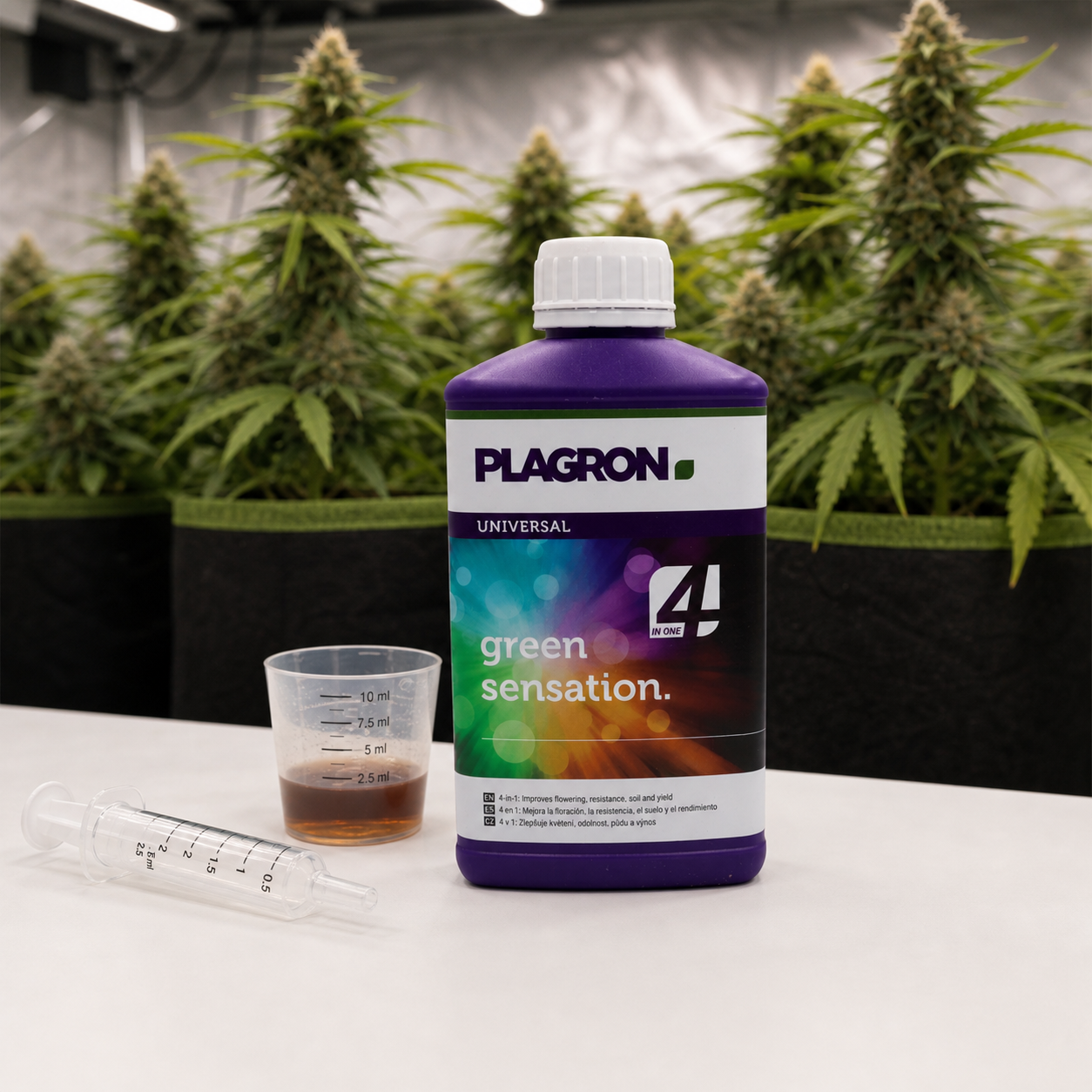 Botella de Green Sensation de Plagron junto a un vaso graduado con líquido y una jeringa, con plantas de cannabis al fondo.