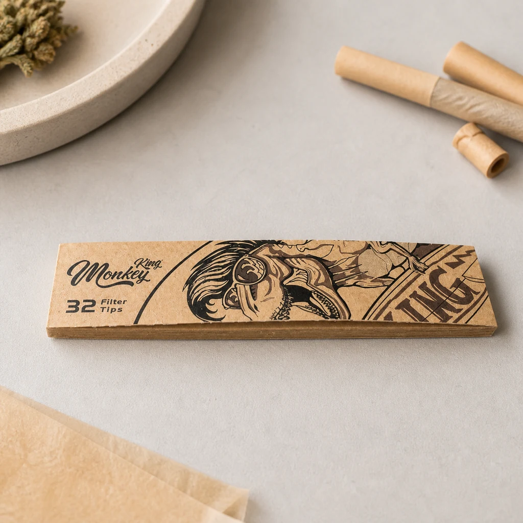 Estuche Monkey King de 32 filtros con dibujo de un mono con gafas, sobre una mesa junto a papeles y boquillas enrolladas.